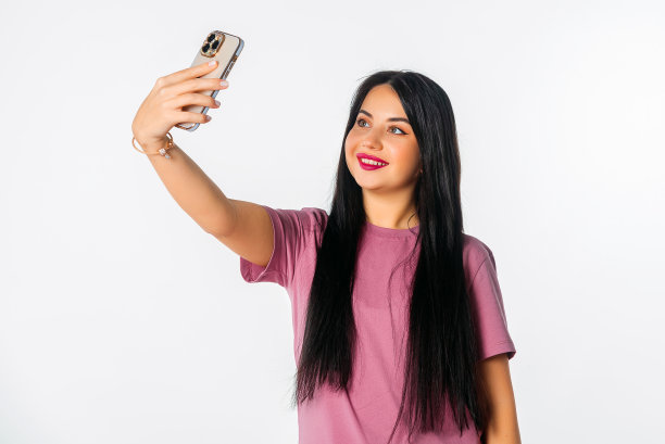 可爱的年轻女子手持智能手机，使用手机应用程序进行视频通话或自拍照片，站在白色的工作室背景下图片下载