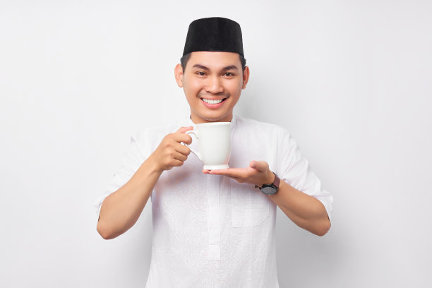 年轻的亚洲穆斯林男子穿着阿拉伯服装，享受着白色背景下的热咖啡或热茶。人们信奉伊斯兰教的生活方式图片下载