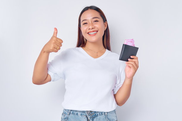 微笑的年轻金发女子女孩亚洲穿着休闲的白色t恤，拿着钱包装满了卢比钞票，显示大拇指孤立在白色背景。人的生活方式概念图片下载