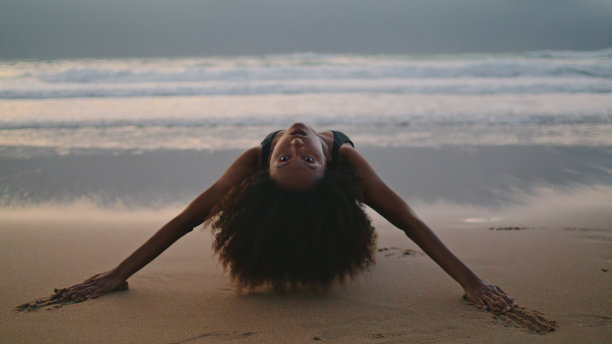 性感的舞者表演海滩躺在黄昏的沙子。女孩弯曲诱人。图片下载