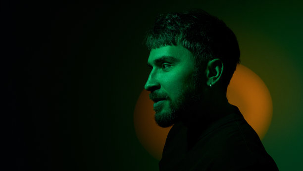 侧视图艺术创意人像男子看在深绿色背景上的橙色霓虹灯。现代照片英俊的胡须中年男子与耳环在耳朵。副本的空间。横幅图片下载