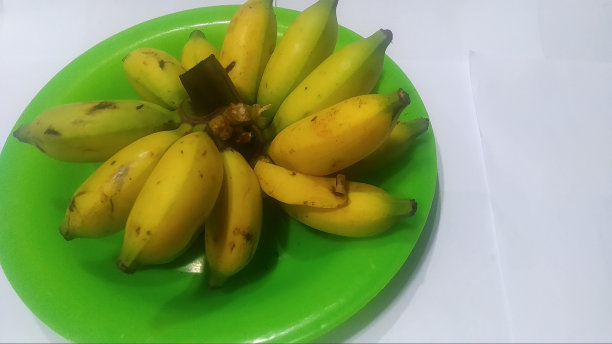 白色背景的绿色塑料碗上的一堆muli香蕉图片下载
