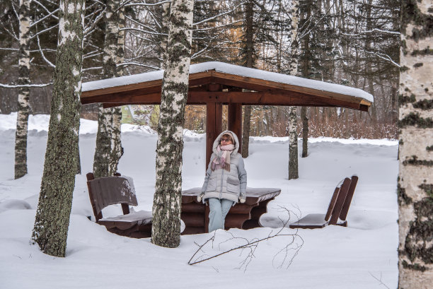在冬季公园的凉亭里，一个穿着暖和衣服的女人正在休息。图片下载