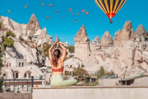 快乐的女孩在土耳其卡帕多西亚做瑜伽练习和冥想，背景是热气球图片下载