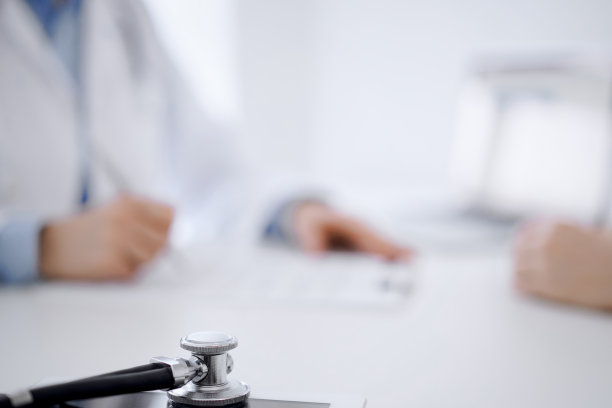 听诊器放在平板电脑上，医生和病人面对面坐在后面。医学、保健概念图片下载