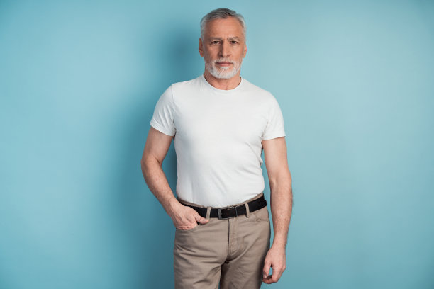 一位年长的男子站在一堵蓝色墙壁的背景上。有吸引力的，严肃的男人在休闲服装隔离在空白的墙壁背景。图片下载