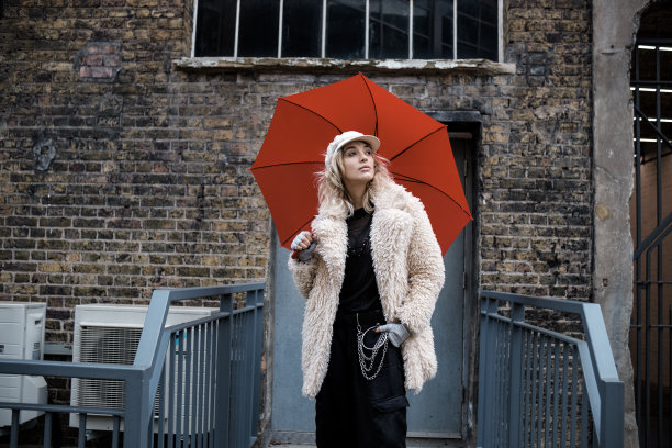 拿着红伞的女人站在老建筑前。图片下载