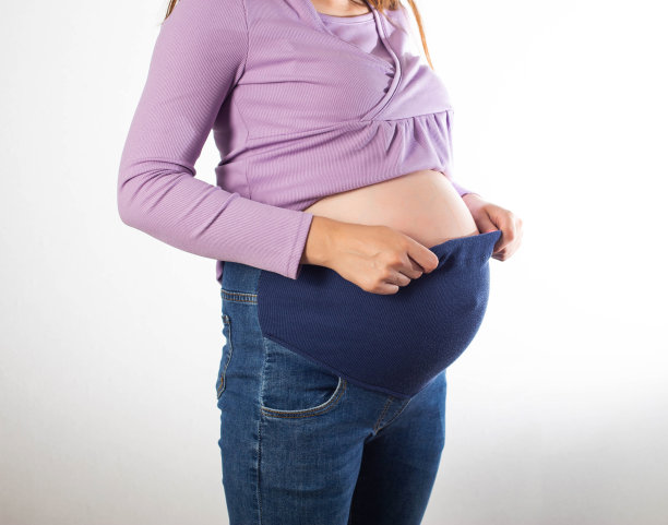 一个穿着白色背景牛仔裤的大肚子孕妇。孕妇舒适的服装概念，通用的弹力牛仔裤。图片下载