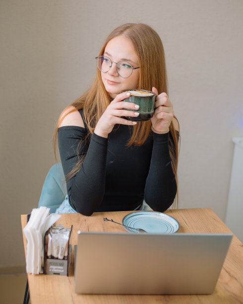 一位穿黑色上衣的年轻女子在咖啡馆里做自由职业。女学生在远程工作喝咖啡。图片下载