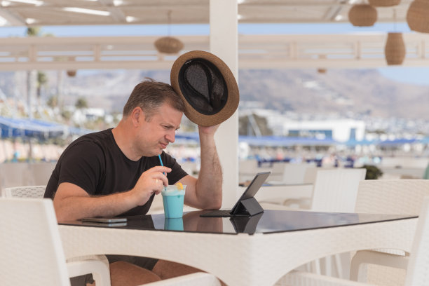 皱着眉头的人在数字平板电脑上工作时摘下帽子图片下载