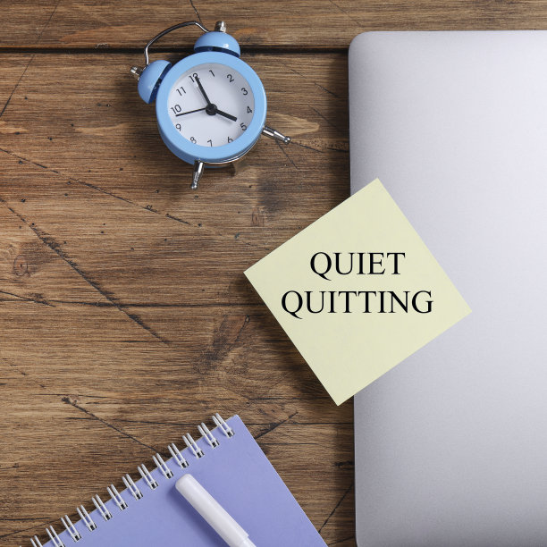在带有时钟和笔记本电脑的黄色贴纸上引用“安静地辞职”。工作与生活平衡的概念。后疫情时代的生活哲学。广场图片下载