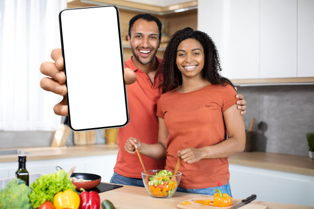 快乐的千禧一代非洲裔美国夫妇一起准备有机蔬菜沙拉，展示大号智能手机图片下载