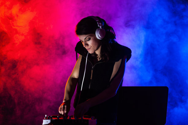 女DJ在混音器上播放音乐。背景是红色和蓝色的灯光和烟雾图片下载