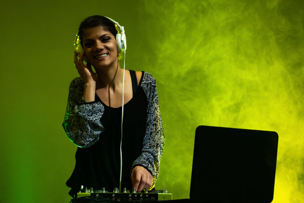 女DJ在调音台上播放音乐。背景是黄色和绿色的烟雾图片下载
