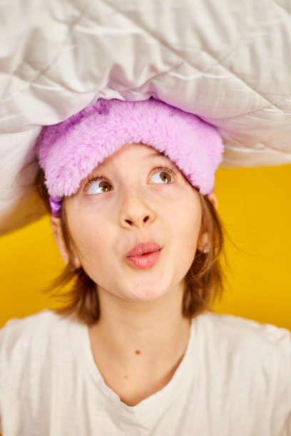 有趣的少女穿着白色睡衣，带着紫色的睡眠面具抱着枕头图片下载