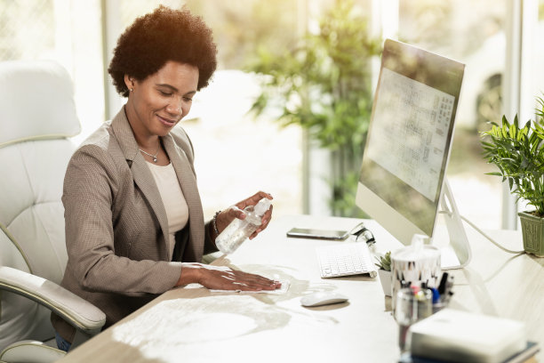 黑人妇女在办公室用杀菌凝胶消毒她的工作工具图片下载