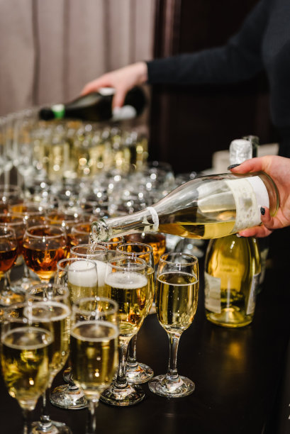 餐饮服务理念。女士们将香槟倒入长笛酒杯中。香槟正被倒入玻璃杯中。侍者们倒着白气泡酒。瓶子的特写视图。一排排满酒杯。图片下载