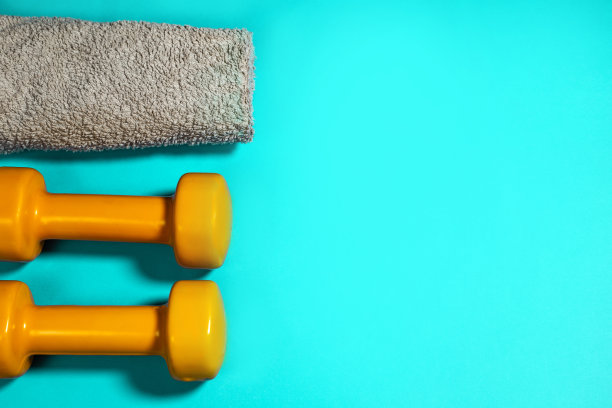两个哑铃桔黄色，灰色毛巾，蓝绿色背景图片下载