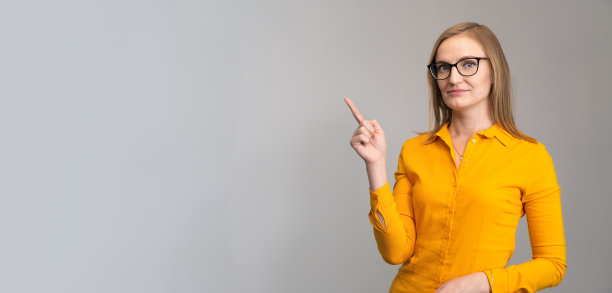 一名戴眼镜、穿橙色衬衫的女子指着浅色背景上的一个空座位。广告、商业、培训的概念。横幅图片下载