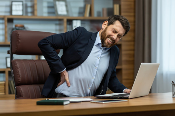 一个年轻的商人坐在办公室的桌子旁，扶着他的背，按摩他的手。遭受平底锅，压力，抽筋。痛得畏缩图片下载