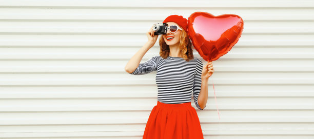 夏天的肖像快乐微笑的年轻女子与电影相机和红色心形气球戴贝雷帽在白色背景图片下载