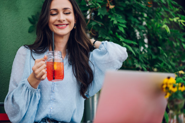 一名女子坐在街边咖啡馆边喝冷饮边用笔记本电脑图片下载