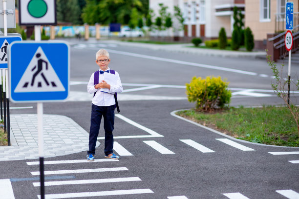 一个戴着眼镜、背着背包的金发男孩在人行横道上上学。知识日图片下载