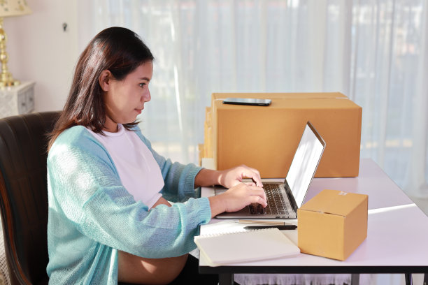 有吸引力的快乐亚洲孕妇坐着，使用移动智能手机，用电脑为客户订购。准妈妈在怀孕期间为孩子的出生做准备和工作图片下载