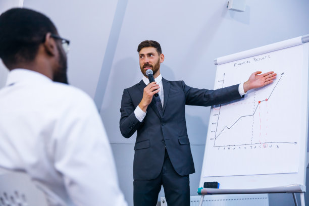 西装革履的男商务教练讲师正在进行白板演示，讲师为客户群体员工进行咨询培训。图片下载
