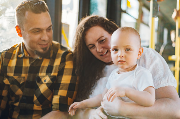快乐的父母和儿子坐在公共汽车上，婴儿坐在母亲的大腿上。图片下载