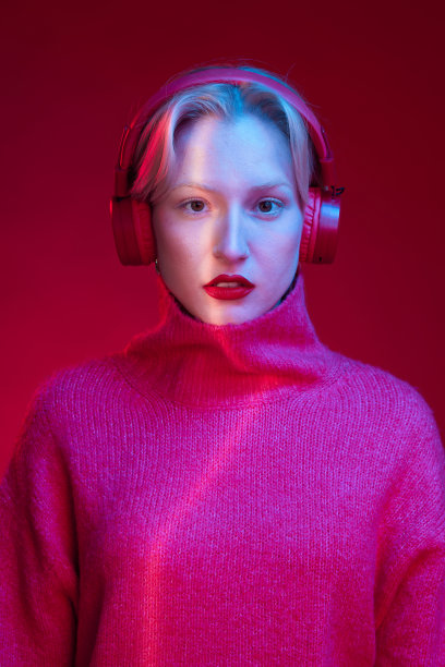一个严肃的女人一边听着音乐，一边看着被隔离在洋红色背景上的相机。洋红色万岁，年度流行色。图片下载