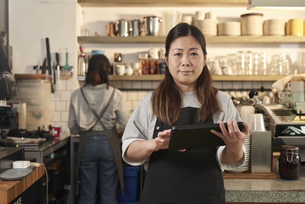 照片中的亚洲咖啡馆老板在咖啡店微笑着拿着无线数码平板电脑。图片下载