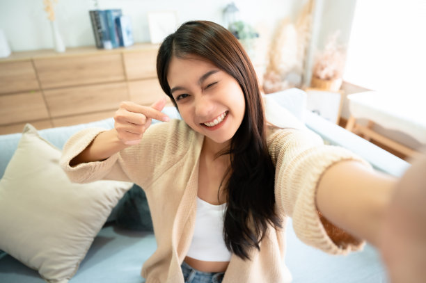 漂亮年轻的亚洲女性，微笑着坐在客厅里。她在模糊的背景下愉快地自拍图片下载