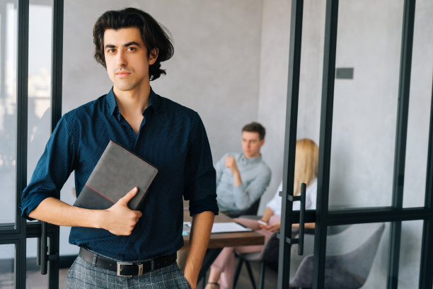 画像英俊的商人手里拿着时髦的纸笔记本文件站在办公室，看着相机。图片下载