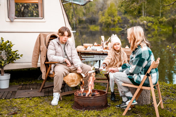孩子，家人，哥哥姐姐在火上煎棉花糖。在大自然中野餐。木制椅子、桌子。烧烤烧烤食物。假期旅游，假期周末聚餐。路上的午餐小吃。露营车，带轮子的房子，拖车图片下载