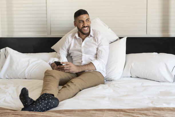 商人躺在酒店的床上，看着智能手机上的信息，一边思考一边微笑图片下载
