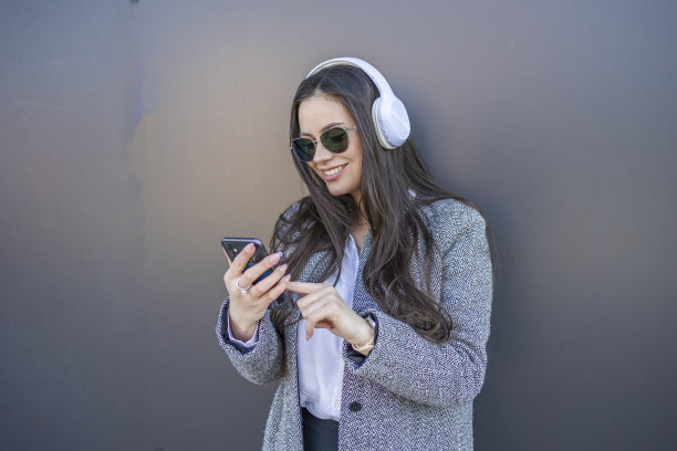 美丽的女人戴着耳机在她的耳朵上听音乐在她的手机。图片下载