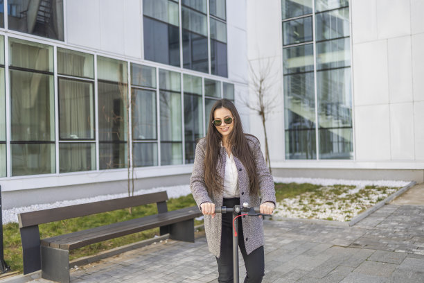 每小时更多的微笑。一个时尚的女孩微笑着沿着城市骑电动滑板车的肖像。图片下载