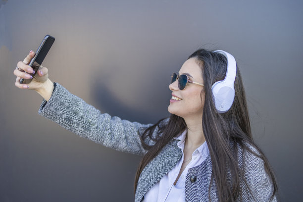戴着耳机的美女用手机拍照。图片下载
