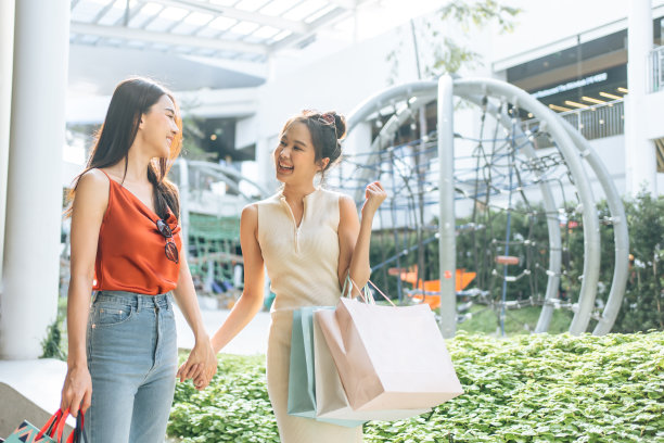 亚洲年轻的两名女子在百货公司户外购物。美丽的女人拿着购物袋，然后幸福地独自行走，享受在百货公司或购物中心购买。图片下载