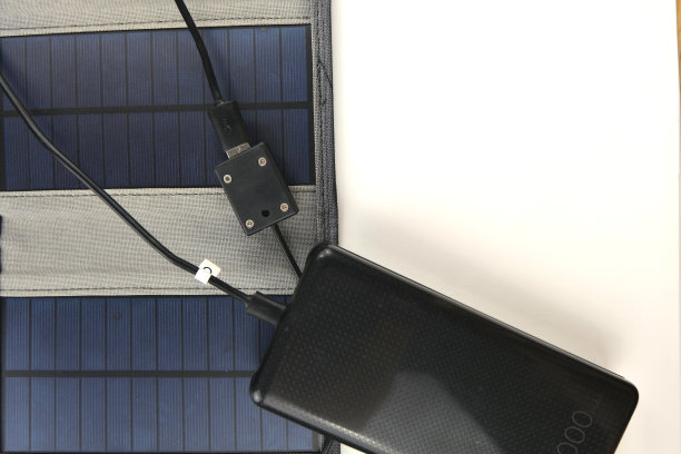 一个巨大的黑色充电宝正在用白色背景的便携式太阳能板充电图片下载