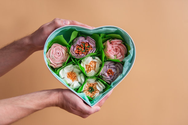 在橙色孤立的背景下，男性手握心形礼盒与甜蜜的棉花糖花。图片下载