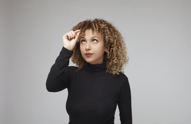 年轻的卷发女子看着一绺头发，她正拿着她的手。图片下载