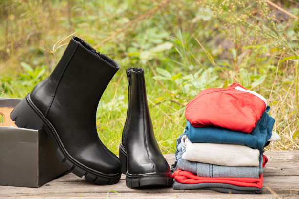女式厚底黑高筒靴和一堆东西站在木板上晒太阳，女式鞋子和冬装，时髦的衣服和鞋子图片下载