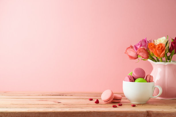 马卡龙法式曲奇放在木桌上，粉色背景上有玫瑰花束。图片下载