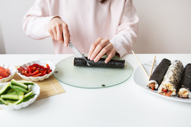 在制作寿司的过程中，女孩用不同的口味制作寿司——新鲜的鲑鱼、鱼子酱、鳄梨、黄瓜、生姜、米饭。把面包卷切成小块。图片下载