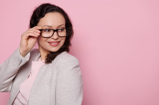 华丽的女人，戴着黑色框架眼镜，微笑着看着旁边的广告空间在粉红色的背景。人。光学。风格图片下载