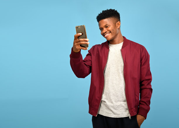 当地非洲男子在一个可隔离的蓝色工作室背景前自拍，通过他的智能手机相机图片下载