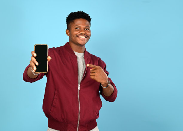 兴奋的商务男子在休闲飞行员夹克展示他的手机与空白屏幕，孤立在蓝色背景图片下载