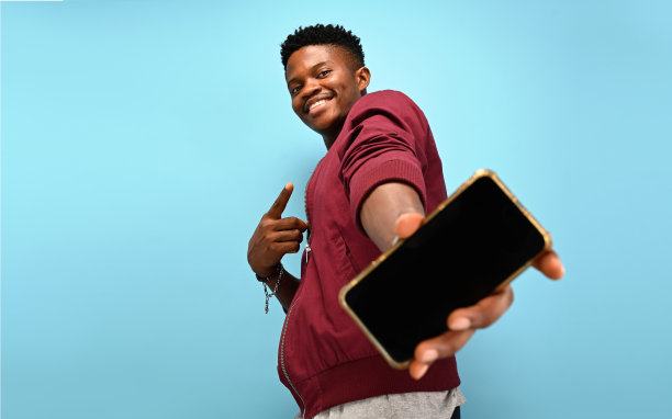 照片肖像年轻的家伙指着手机屏幕与文案空间穿着红酒开衫孤立在蓝色背景图片下载